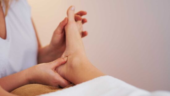 Practitioner applying targeted pressure to specific zones on patient's bare foot using reflexology techniques.